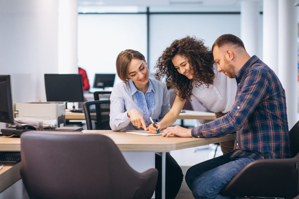Tres personas colaborando en una oficina, revisando documentos y tomando notas en una mesa de trabajo.